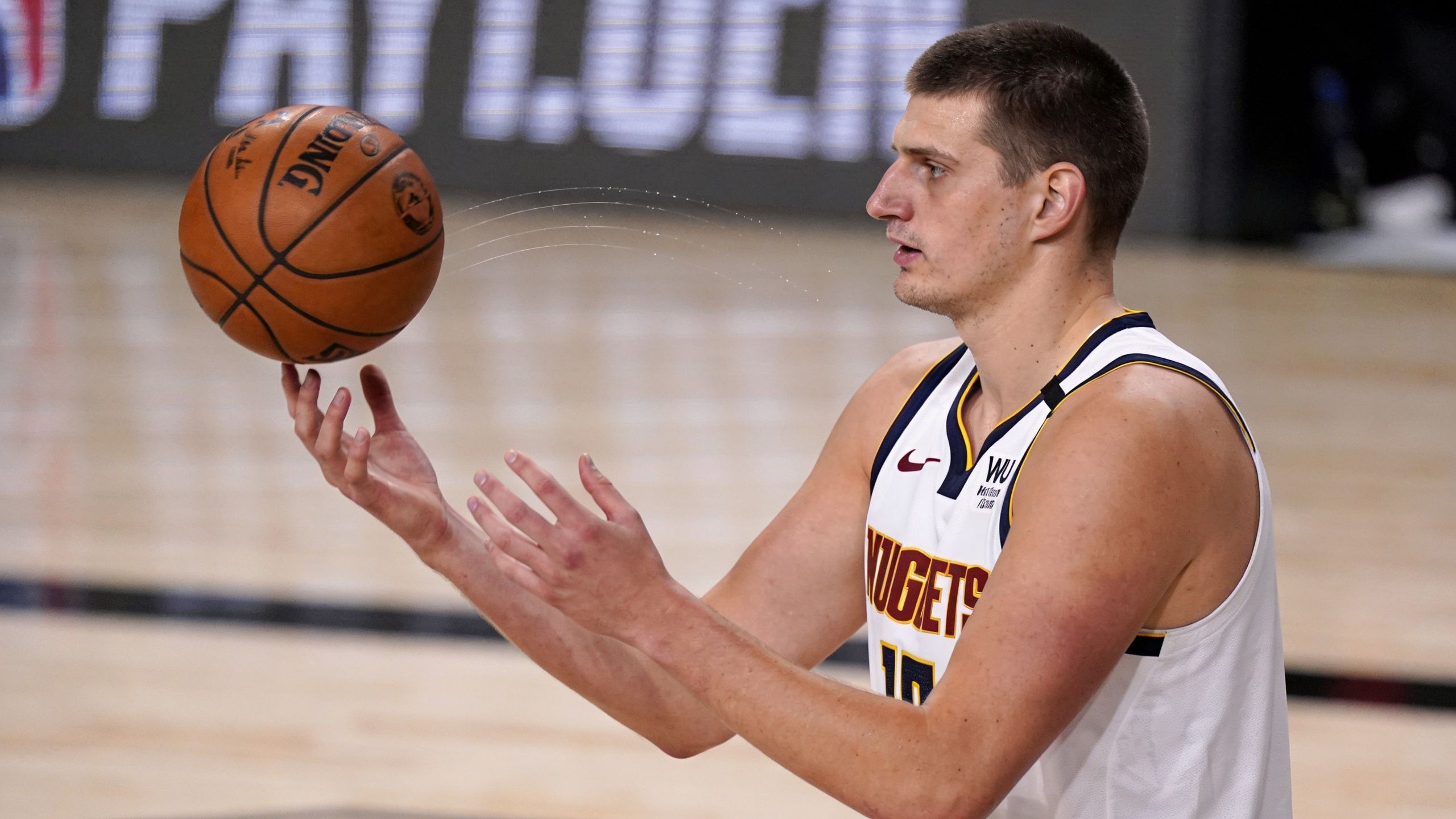 Denver Nuggets basketball player Nikola Jokic skillfully balancing a basketball on his fingertips during a game.